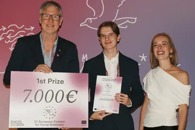 Trzy osoby pozują na scenie podczas ceremonii wręczenia nagród 37. edycji European Contest for Young Scientists w Kiel 2026, środkowa osoba trzyma dyplom za pie